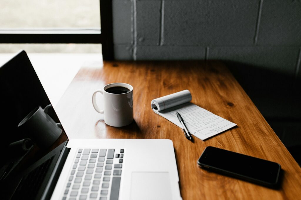 a wooden desk with a laptop and notepad and pen representing blogging, that is, one of many unique ways to make money without investment 