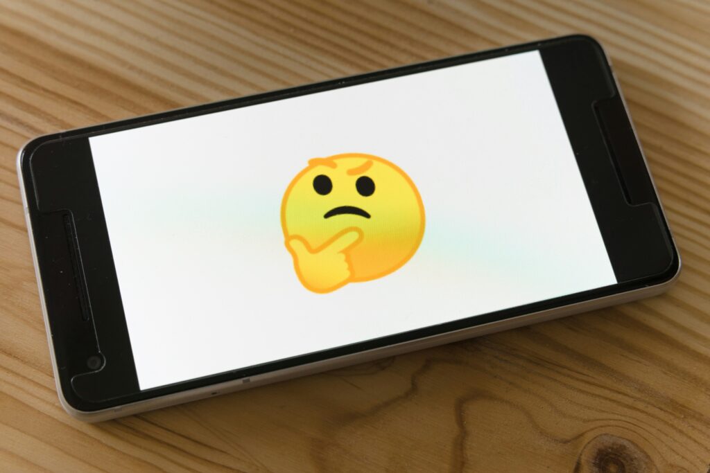 A phone in landscape mode with a yellow emoji showing the expression of thinking. 